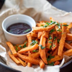 Close-up of crispy sweet potato fries garnished with parsley served with a dip.